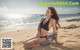 A woman in a black bikini sitting on a beach.