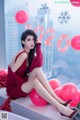 A woman in a red dress sitting on a window sill with red balloons.