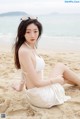 A woman in a white bikini sitting on the beach.