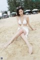 A woman in a white bikini sitting on the sand.