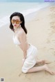 A woman in a white bikini sitting on the beach.