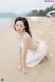 A woman in a white dress kneeling on a beach.