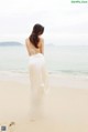 A woman in a white dress walking on the beach.