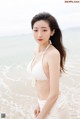 A woman in a white bikini standing on the beach.