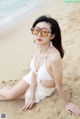 A woman in a white bikini sitting on the beach.