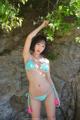 A woman in a blue bikini posing in front of a rock.