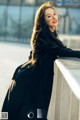 A woman in a black coat leaning against a railing.