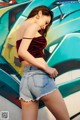 A woman in a red top and denim shorts posing in front of a graffiti wall.