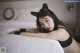 A woman laying on a bed wearing a black cat ears headband.