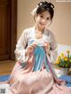 A woman in a pink and blue hanbok sitting on a bed.