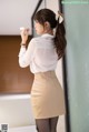 a woman in a white shirt and tan skirt leaning against a wall