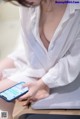 A woman in a white shirt is looking at her phone.