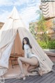 A woman sitting in front of a teepee on a wooden deck.