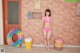 A woman in a pink bikini standing next to a brick wall.