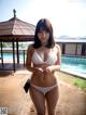 A woman in a white bikini standing next to a pool.