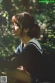 A woman in a school uniform sitting in the woods.