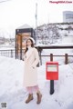 A woman standing next to a red post box in the snow.