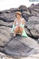 A woman sitting on top of a large rock on the beach.