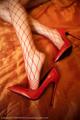 A woman wearing red fishnet stockings and high heels on a bed.