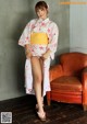 A woman in a kimono standing next to a red chair.