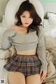 a woman in a gray sweater and plaid skirt sitting on a bed