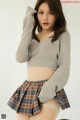 a woman in a gray sweater and plaid skirt posing for a picture