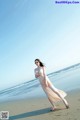 A woman in a long dress walking on the beach.