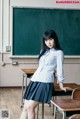 A woman in a school uniform standing in front of a blackboard.