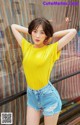 A woman in a yellow shirt and denim shorts posing for a picture.