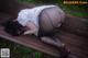 A woman in a white shirt and black stockings laying on a wooden bench.