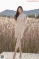 A woman in a beige sweater dress standing on a wooden platform.