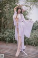 A woman in a white robe is posing on a wooden deck.