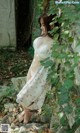 A woman in a white dress leaning against a wall.