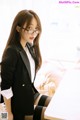 A woman in a black suit and glasses sitting at a table.