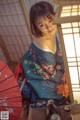 A woman in a blue kimono sitting at a table with an umbrella.