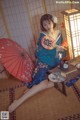 A woman in a blue kimono sitting on the floor with a red umbrella.