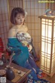 A woman in a blue kimono sitting next to a lamp.