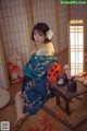 A woman in a blue and orange kimono sitting on the floor.