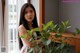 A woman standing next to a plant in front of a window.