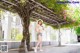 A woman in a white top and shorts standing under a tree.