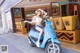 A woman sitting on a blue scooter in front of a store.