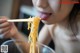 A woman eating noodles with chopsticks in her mouth.