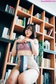 A woman sitting on top of a book shelf holding a book.