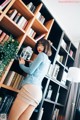 A woman standing in front of a bookshelf holding a cell phone.