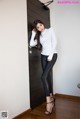 A woman in a white shirt and black leggings leaning against a door.