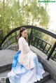 A woman in a blue and pink hanbok sitting on a bridge.