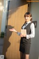 A woman in a black skirt and white shirt is holding a book.