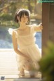 A woman in a white dress sitting on a wooden floor.