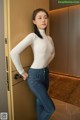 A woman in a white top and jeans leaning against a door.