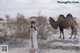 A woman in a white dress standing next to a camel.